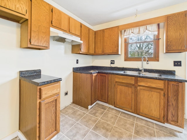 kitchen featuring under cabinet range hood, light tile patterned floors, brown cabinets, and a sink