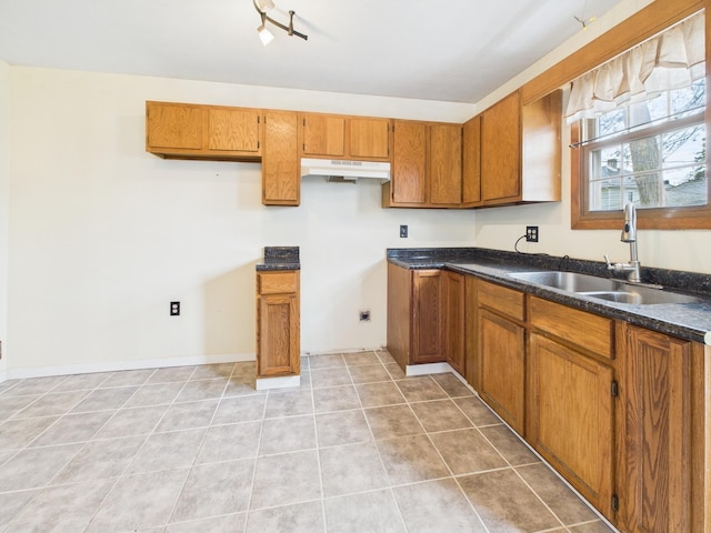 kitchen with a sink, light tile patterned floors, under cabinet range hood, and brown cabinets