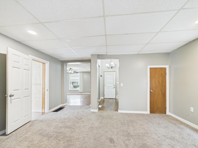 carpeted empty room featuring an inviting chandelier, baseboards, and a drop ceiling
