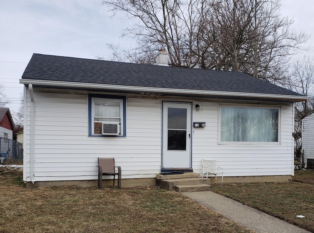 view of front of house with a shingled roof, entry steps, a chimney, and a front yard