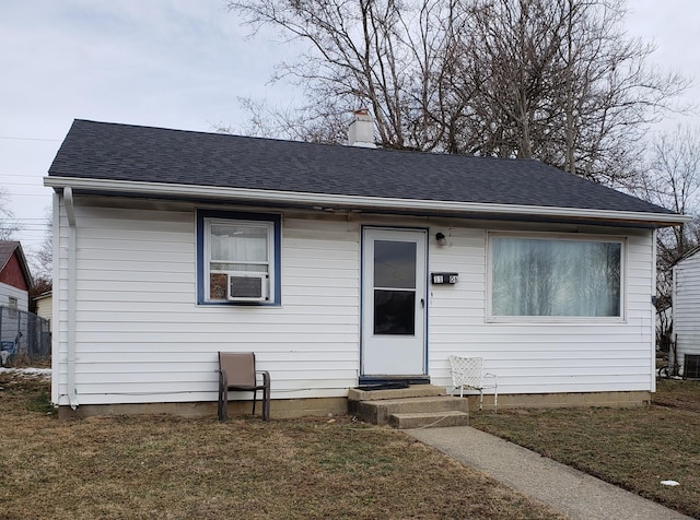 view of front of house with a shingled roof, entry steps, a chimney, and a front yard