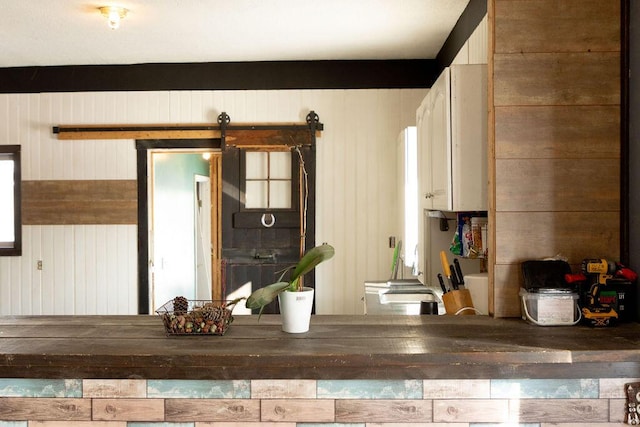 kitchen with white cabinetry, a barn door, and wood walls