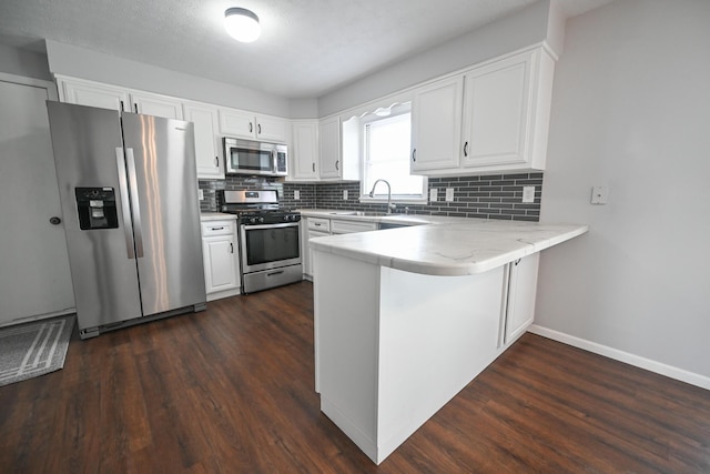kitchen featuring decorative backsplash, a peninsula, white cabinetry, dark wood finished floors, and appliances with stainless steel finishes