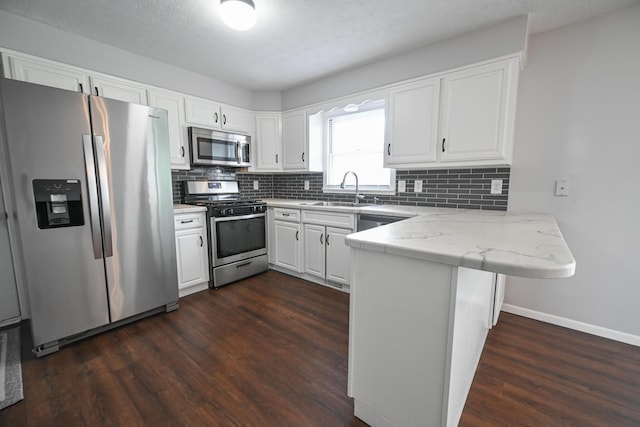 kitchen featuring dark wood-style flooring, appliances with stainless steel finishes, a sink, a peninsula, and white cabinetry