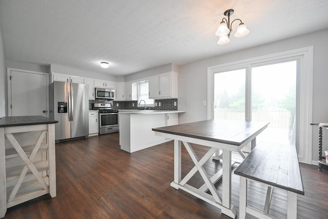 kitchen featuring white cabinets, a sink, stainless steel appliances, a peninsula, and backsplash