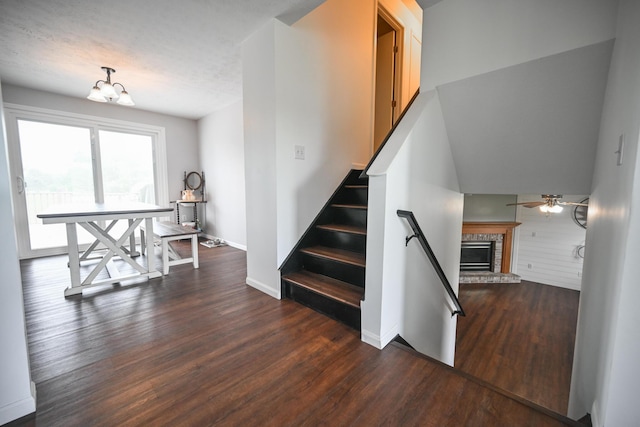 stairs featuring ceiling fan with notable chandelier, baseboards, a stone fireplace, and wood finished floors