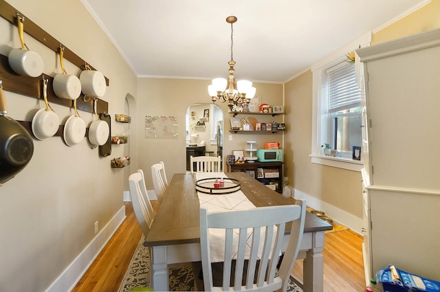 dining area with an inviting chandelier, ornamental molding, and light wood-type flooring