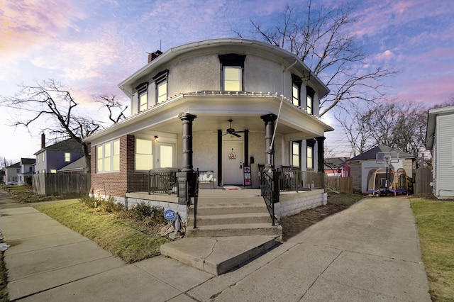 view of front facade with brick siding, stucco siding, a porch, fence, and ceiling fan