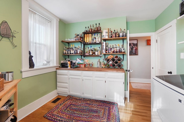 bar with white cabinets and light hardwood / wood-style flooring