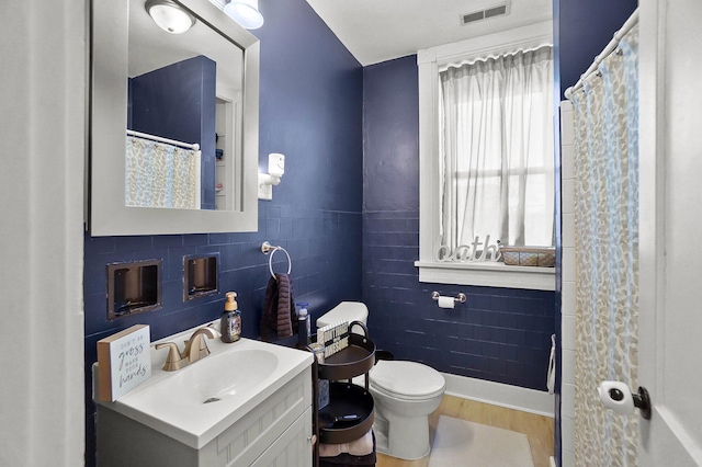 bathroom featuring wood-type flooring, tile walls, vanity, and toilet