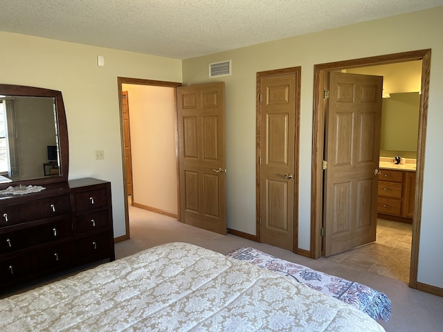 bedroom featuring visible vents, a textured ceiling, ensuite bath, baseboards, and light colored carpet