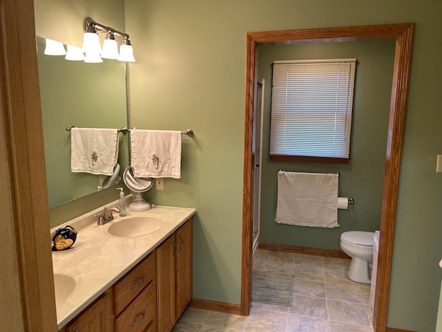 full bathroom with double vanity, toilet, baseboards, and a sink
