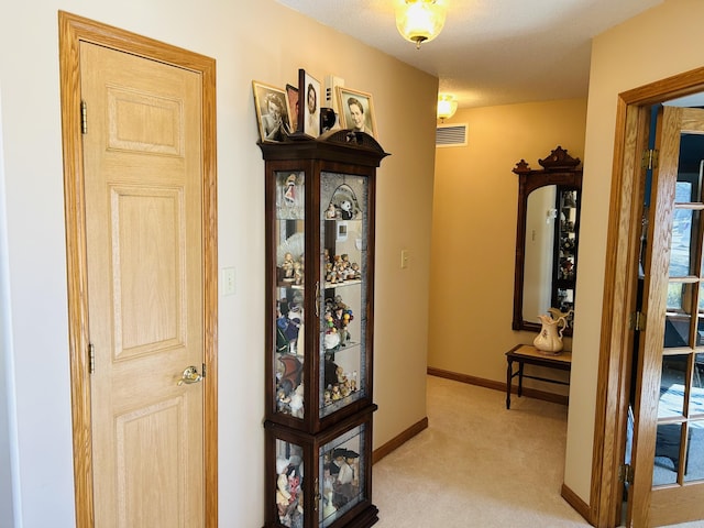 hall with visible vents, baseboards, and light colored carpet