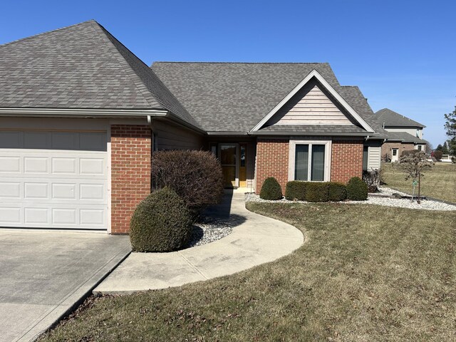 ranch-style home with brick siding, an attached garage, a front yard, and roof with shingles