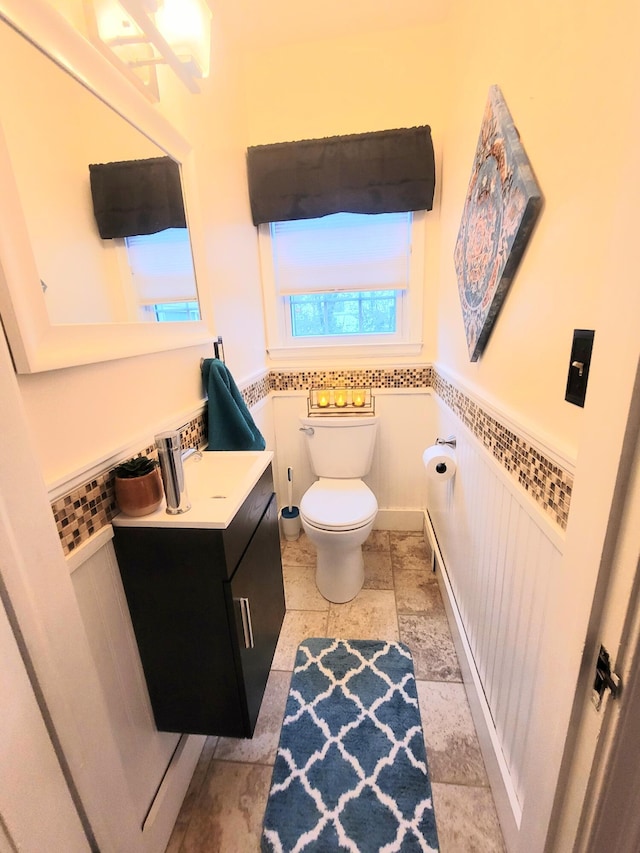 bathroom featuring a wainscoted wall, toilet, vanity, and stone finish flooring