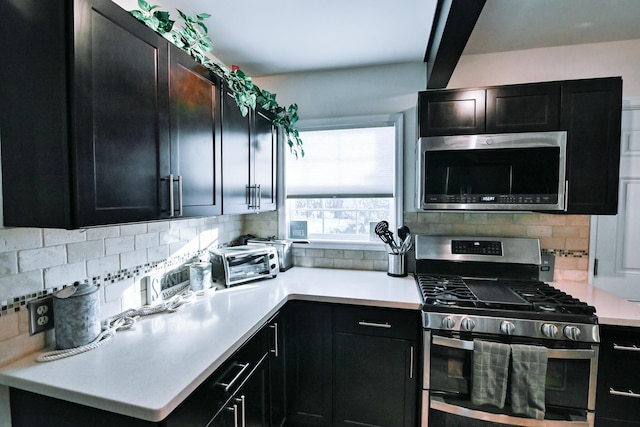 kitchen featuring tasteful backsplash, a toaster, light countertops, appliances with stainless steel finishes, and dark cabinetry