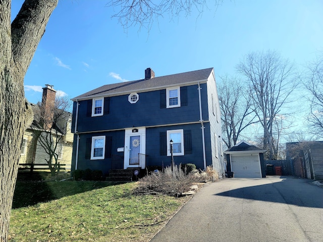 colonial house with fence, a chimney, an outdoor structure, a front lawn, and a garage