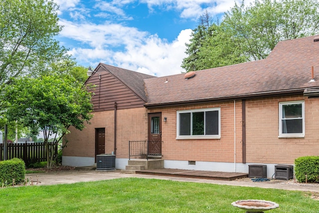 rear view of house featuring roof with shingles, fence, a yard, central AC, and brick siding