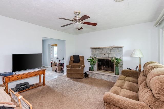 living room featuring carpet, a ceiling fan, a textured ceiling, and a stone fireplace