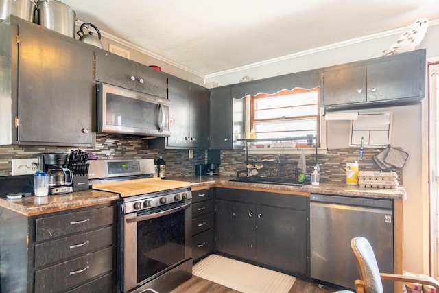 kitchen featuring appliances with stainless steel finishes, ornamental molding, wood finished floors, a sink, and backsplash