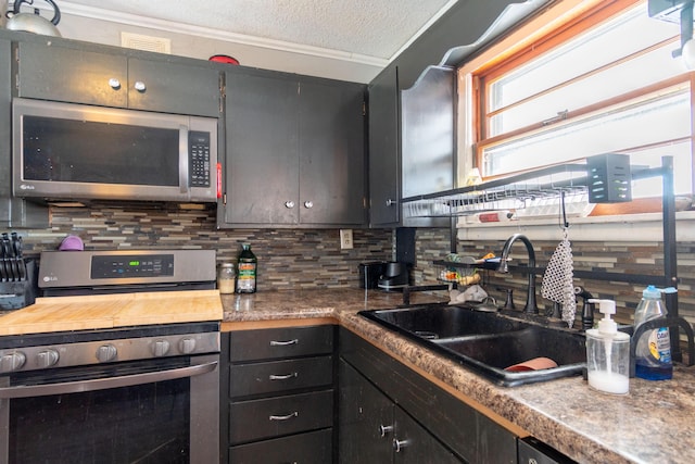 kitchen with appliances with stainless steel finishes, a sink, crown molding, a textured ceiling, and backsplash