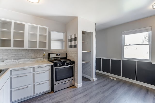 kitchen with light countertops, light wood-style flooring, white cabinets, and stainless steel gas range oven