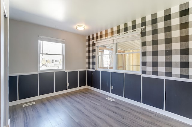 empty room with wood finished floors, visible vents, and wainscoting