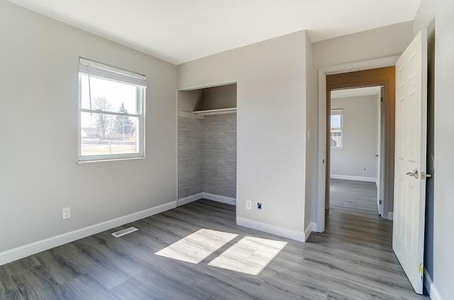 unfurnished bedroom featuring visible vents, baseboards, a closet, and wood finished floors