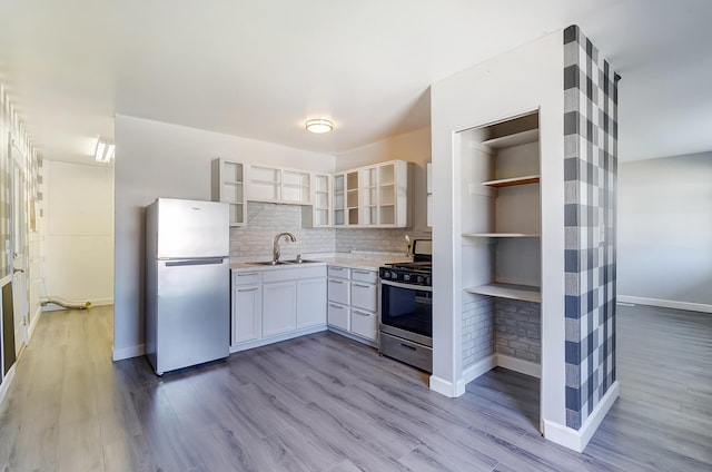 kitchen featuring light wood-type flooring, open shelves, a sink, tasteful backsplash, and stainless steel appliances