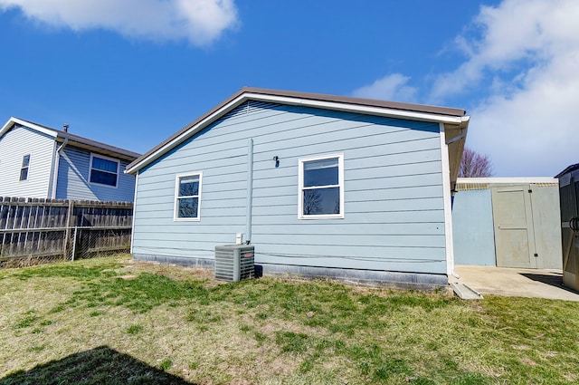 back of house with an outbuilding, central air condition unit, a lawn, and fence