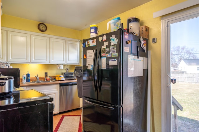 kitchen with light wood-style flooring, freestanding refrigerator, stainless steel dishwasher, white cabinetry, and a sink