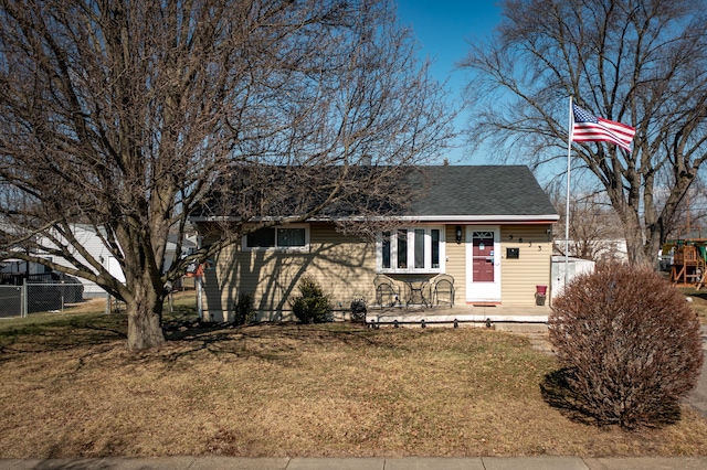 view of front of property featuring roof with shingles, fence, and a front lawn