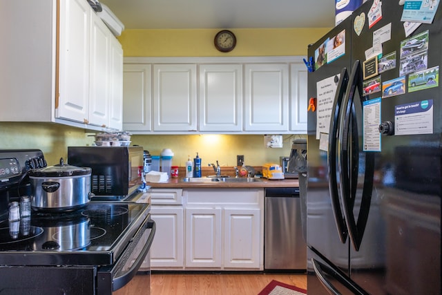 kitchen with light wood-style floors, white cabinets, a sink, and black appliances