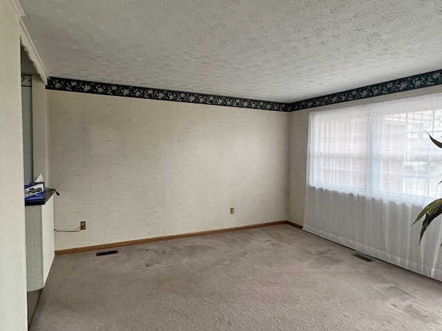 carpeted empty room featuring a textured ceiling, visible vents, and baseboards