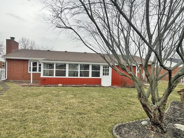 back of house featuring a sunroom, brick siding, a chimney, and a lawn