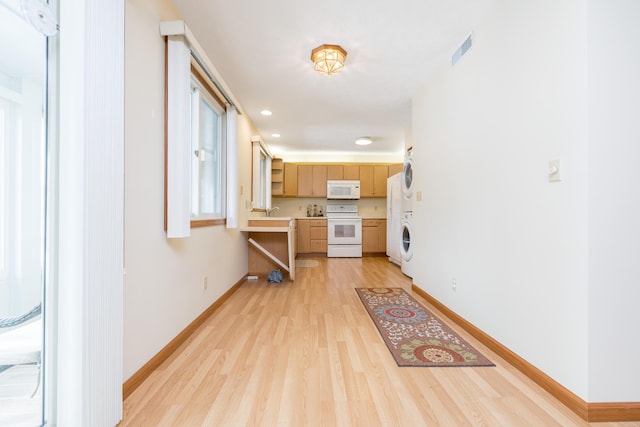 kitchen with stacked washer and dryer, white appliances, sink, light hardwood / wood-style floors, and light brown cabinetry