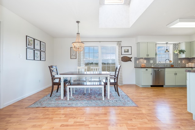 dining space with a notable chandelier, a skylight, light hardwood / wood-style floors, and sink