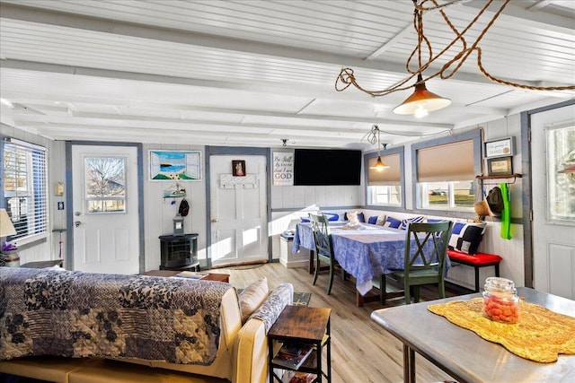 living room featuring beam ceiling, a healthy amount of sunlight, a wood stove, and wood finished floors