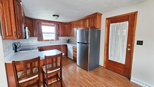 kitchen with sink, appliances with stainless steel finishes, a baseboard heating unit, backsplash, and light wood-type flooring