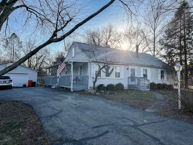 view of front facade with aphalt driveway, a porch, an outdoor structure, a garage, and a chimney