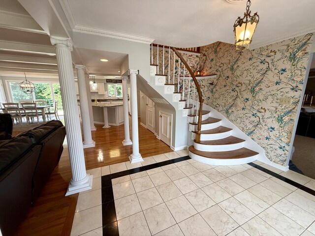 1337 Stratford Dr, Piqua, OH 45356 - stairway featuring ornate columns, inlaid floor details, baseboards, crown molding, and a chandelier