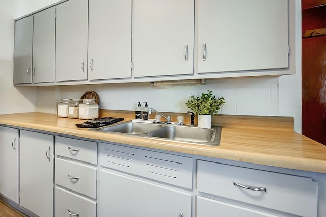 kitchen with tasteful backsplash, white cabinets, light countertops, and a sink