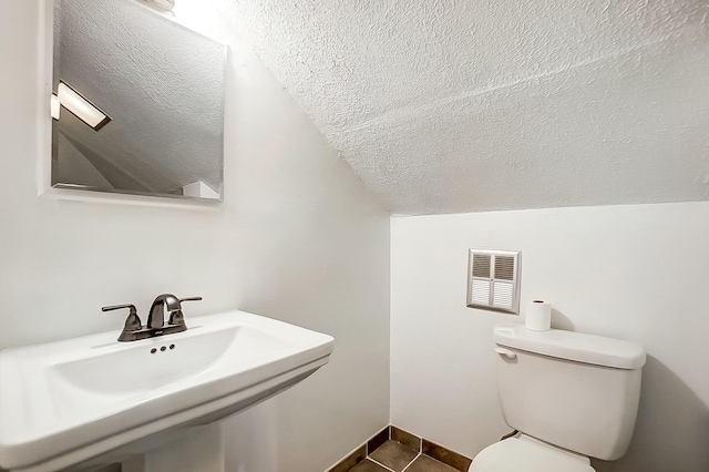 half bath featuring visible vents, toilet, vaulted ceiling, a sink, and a textured ceiling