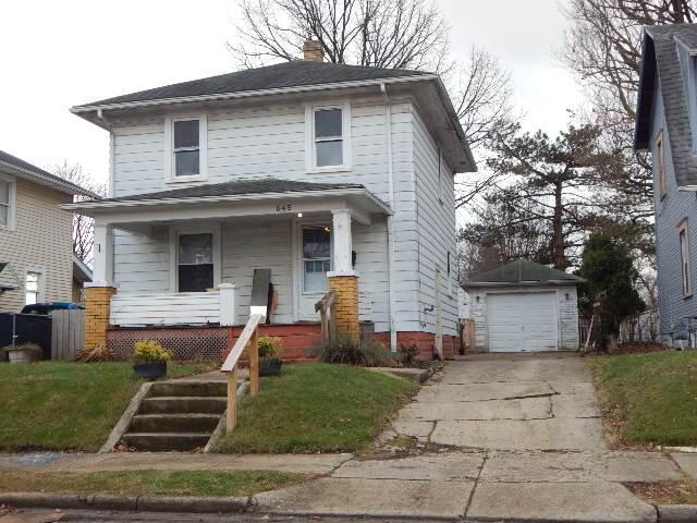 american foursquare style home featuring a front lawn, driveway, covered porch, an outdoor structure, and a chimney