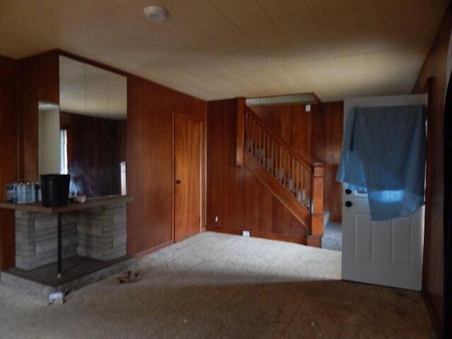 living room with carpet flooring, wood walls, and stairs