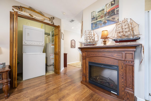 interior space with visible vents, stacked washer and dryer, laundry area, wood finished floors, and gas water heater