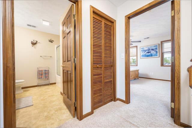 corridor with visible vents, baseboards, and light colored carpet