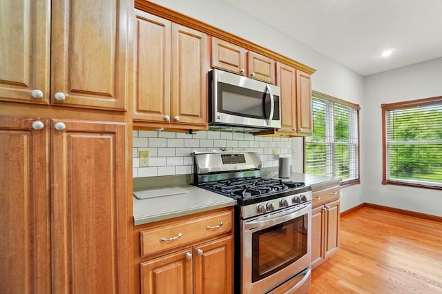kitchen with appliances with stainless steel finishes, backsplash, baseboards, light wood-style floors, and brown cabinets