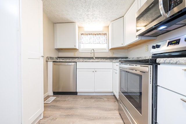 kitchen featuring visible vents, white cabinets, a sink, light wood-style flooring, and appliances with stainless steel finishes