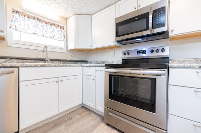 kitchen featuring white cabinetry, appliances with stainless steel finishes, a sink, and light wood-style floors